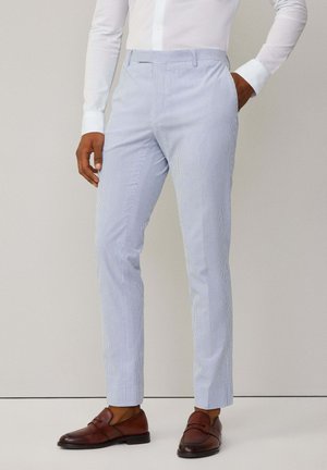 Pantaloni a righe blu chiaro realizzati in tessuto con una texture liscia, caratterizzati da una vestibilità slim e frontale piatto. Indossati con scarpe in pelle marrone.