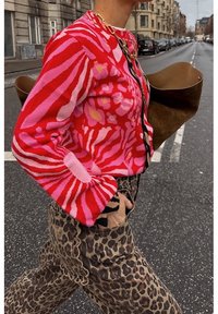 Cárdigan a rayas rojas y rosas con tejido texturizado, combinado con pantalones de estampado de leopardo con bordes con volantes y un bolso marrón de gran tamaño.