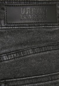 Mustast nahast silt tumehallidel teksapükstel, millele on pressitud tekst "Urban Classics Denim Factory".