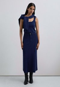 Top de punto sin mangas color azul marino combinado con una falda midi a juego, que cuenta con una cintura con detalle de botón, y botas negras hasta la rodilla.