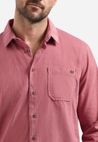 Lange mouwen, knoopshirt in vervaagd roze stof met een zak en contrasterende knopen. Zachte textuur met een casual ontwerp.
