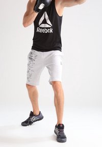 Black Reebok tank top with logo, gray shorts with a textured pattern, and black athletic shoes with red accents. Boxer stance with gloves.