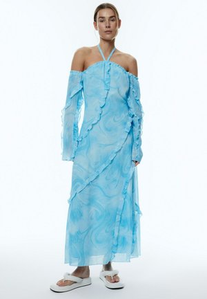 Blauwe, semi-transparante maxi-jurk met off-shoulder ontwerp, gerimpelde randen en marmerpatroon, gecombineerd met witte platform sandalen.