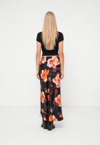 Zwarte maxi rok met oranje bloemenprint, gladde stof, uitlopende ontwerp, gedragen met een aansluitend zwart topje en zwarte chunky laarzen.