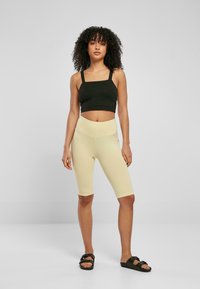 Zwarte cropped tanktop met brede banden, gecombineerd met lichtgele fietsshorts. De shorts zijn aansluitend en hebben een tailleband die ontworpen is voor comfort.