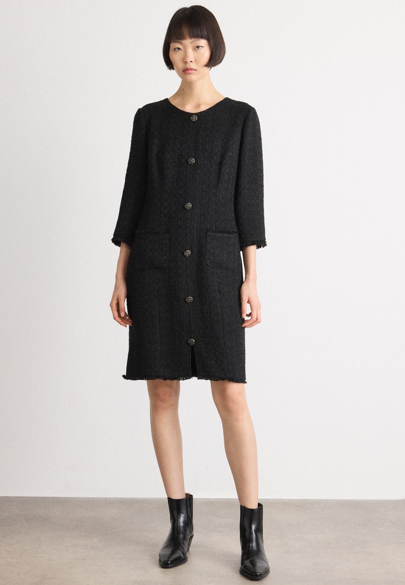 Abito in tweed nero con scollatura tonda, maniche lunghe, sei bottoni davanti e due tasche frontali. Orlo sfrangiato e tessuto texture.