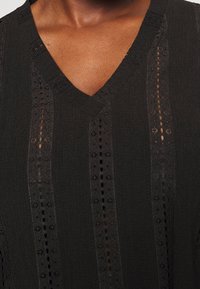 Haut en maille de couleur foncée avec col en V, design à rayures verticales et détails complexes avec motifs texturés et découpes.