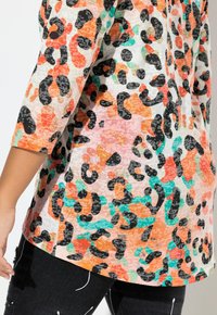 Top con stampa leopardata caratterizzata da un motivo testurizzato in arancione, nero e teal su una base crema, con maniche a tre quarti e orlo stondato.