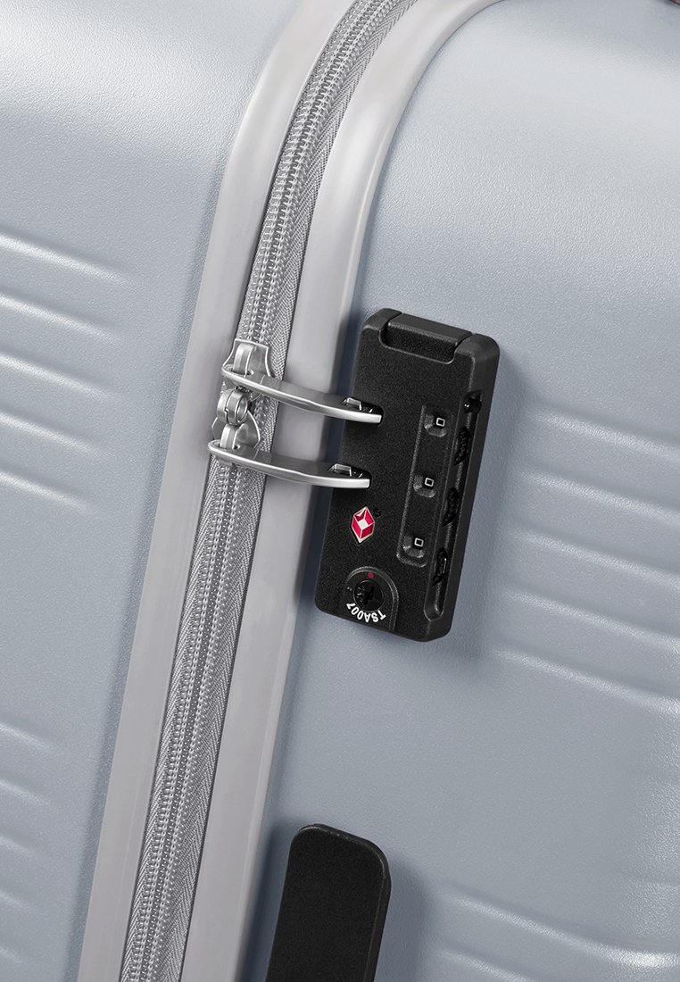 Maleta rígida gris con cremallera plateada. Contiene un candado TSA negro con logo rojo, un dial de combinación de 3 dígitos y accesorios de metal.