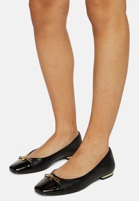 Czarne skórzane baletki z zaokrąglonym noskiem, błyszczącym lakierowanym czubkiem, złotymi detalami i niskim obcasem.