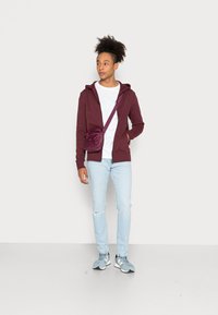 Burgundijos zip-up džemperis, baltas T-shirt, šviesiai mėlyni suplėšyti džinsai ir pilki sportiniai bateliai. Maža burgundinė per petį nešiojama rankinė su dirželiu.