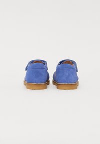 Sapatos de camurça azuis com bico arredondado, tira na parte traseira e sola de borracha castanha. Textura suave com detalhe de costura ao longo das bordas.