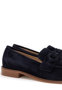 Mocassini in suede blu navy con tacco in legno basso e fibbie decorative in suede, su uno sfondo bianco.