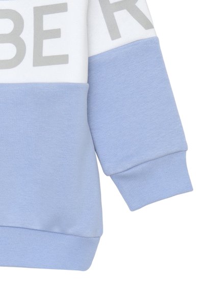 Felpa azzurra chiara con una sezione superiore bianca e lettering grigio in grassetto. Tessuto morbido con polsini a costine e vestibilità rilassata.