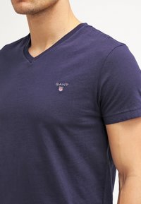 Marineblauw v-hals t-shirt van zachte katoen; heeft een klein geborduurd logo op de borst en korte mouwen. Glad textuur.