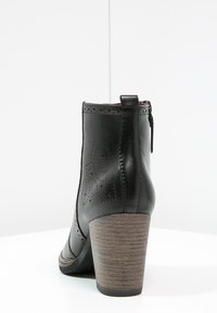 Bottine en cuir noir avec un design perforé, une fermeture éclair et un talon en bois. Texture lisse avec un bout rond. Vue de côté.