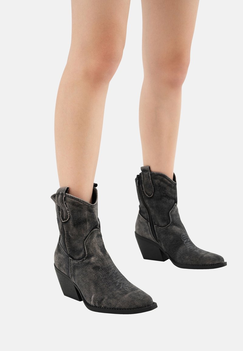 Botas de cuero negras hasta el tobillo con punta afilada, parte superior curvada y tacón cuadrado. Presentan costuras visibles y un acabado texturizado desgastado.