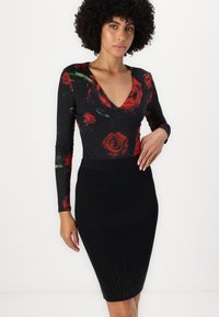 Černý bodysuit s dlouhým rukávem a červeným květinovým vzorem, se špičatým výstřihem, v kombinaci s černou tužkovou sukní s ribbed texturou a třpytivými akcenty na lemu.