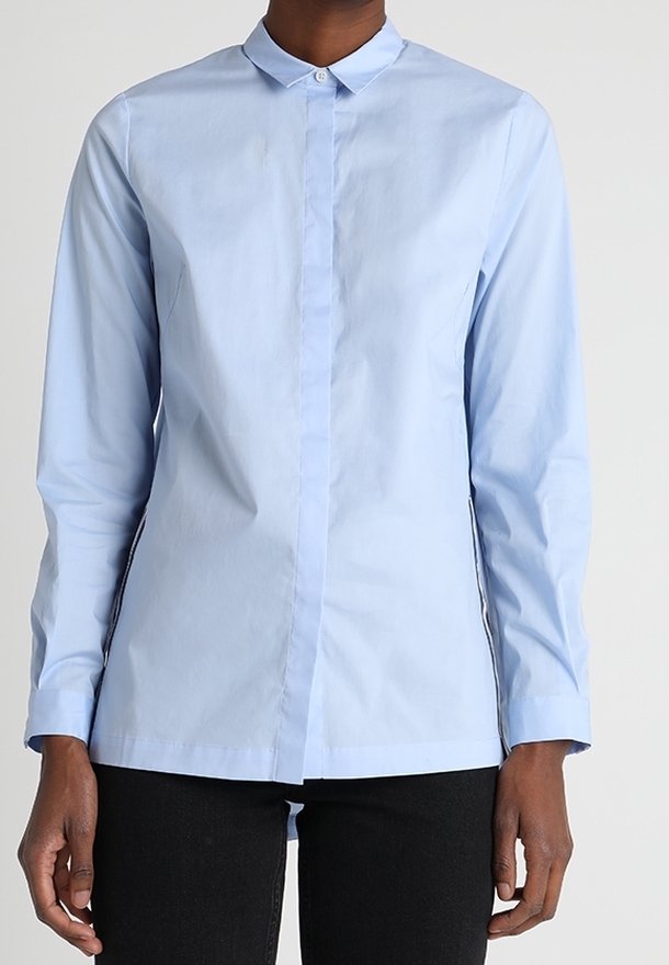 Camicia azzurra a maniche lunghe con colletto abbottonato, taglio dritto e design minimale. Il tessuto sembra liscio; presenta una patta abbottonata nascosta.