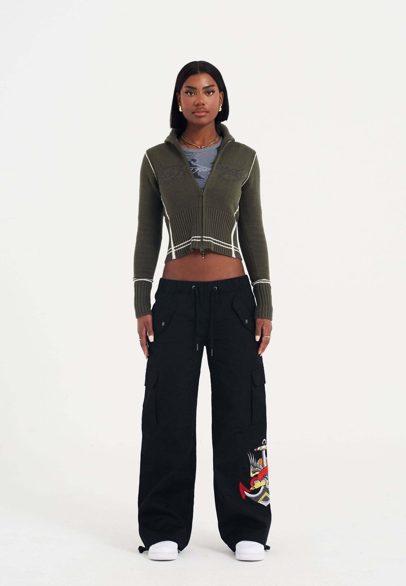 Olijf groene cropped ritssluiting trui met ribbeltextuur, gecombineerd met zwarte cargo broek met zijzakken en kleurrijke geborduurde details.