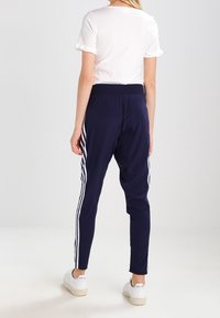 Marina atletiska joggingsbyxor med vita sidostrekar, elastisk midja och en slät textur. Kombinerat med en enkel vit topp och vita sneakers.