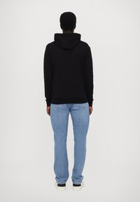 Zwarte hoodie met een gevoerde capuchon, gedragen met lichtblauwe jeans. Stevige sneakers met zwarte zolen maken de casual outfit compleet.