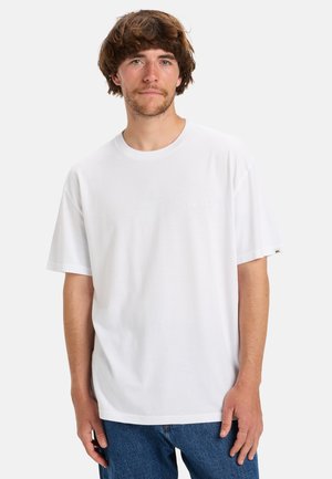 Wit katoenen T-shirt met korte mouwen, ronde halslijn en een subtiele logodetail op de borst. Gemaakt in combinatie met blauwe denim jeans.