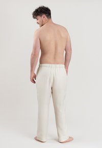 Pantalons blancs, texturés, amples avec une taille élastique, vus de l'arrière. Aucun motif ou détail matériel visible.