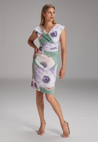 Kukallinen kietoutuva mekko röyhelöhihoilla, jossa on suuret violettia ja vaaleanpunaista kukkakuosia vihreällä taustalla. Silkkinen kangas, polveen ulottuva.
