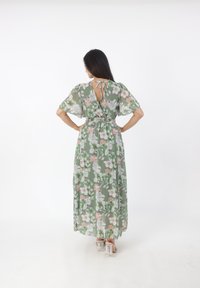 Bloemige maxi-jurk van groene stof met een cinch taille en korte mouwen. Heeft een keyhole rug en een vloeiende, lichte uitstraling.