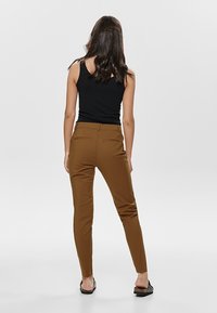Brown fitted pants with a smooth texture, two back pockets, and a mid-rise waist, paired with a black tank top and flat sandals.