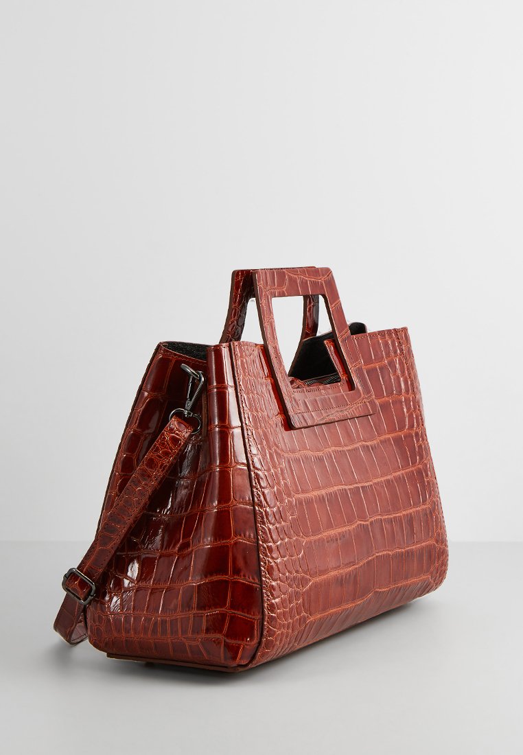 Sac à main en cuir rouge embossé crocodile avec une forme structurée, deux poignées supérieures, et une bandoulière amovible. Présente une finition texturée.