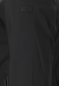 Sort softshell-jakke med struktureret tekstur, der har en lynlås lomme på venstre side og et CMP-logo på brystet.