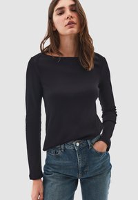 Top nero a maniche lunghe con scollatura a barca, design aderente e texture liscia, abbinato a jeans in denim blu a vita alta.