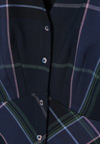 Chemise à carreaux marine avec des accents bleu clair, vert et rose, présentant un col et une fermeture à bouton avec des boutons foncés. Tissu texturé.
