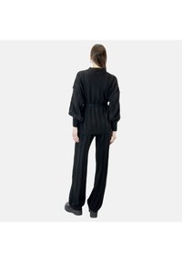 Conjunto de punto negro que incluye un suéter oversized con cinturón y mangas anchas, junto con pantalones de cintura alta a juego, ambos con textura acanalada.