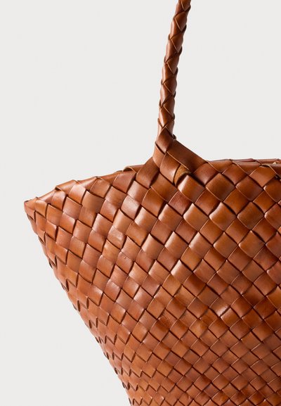 Κοντινή λήψη καφέ δερμάτινης τσάντας tote με υφαντό σχέδιο και πλεγμένη λαβή σε απλό λευκό φόντο.