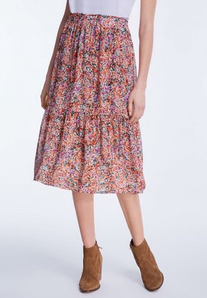 Jupe midi florale dans des teintes d'orange, de rose et de vert, avec un design à volants en étages. Fabriquée en tissu léger. Portée avec des bottines brunes.