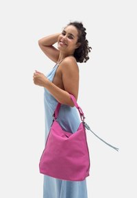 Borsa a tracolla in pelle rosa con finitura testurizzata, caratterizzata da una forma triangolare, tracolla blu regolabile e dettagli di cucitura a contrasto.