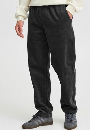 Czarne spodnie kordurojowe o luźnym kroju, z elastycznym pasem i bocznymi kieszeniami, w połączeniu z szarymi trampkami.