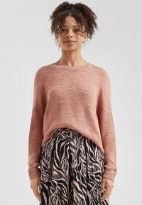Roze gebreide trui met een relaxed fit, textuurstof en geribde manchetten, gecombineerd met een zwarte en roze gestreepte plissérok.
