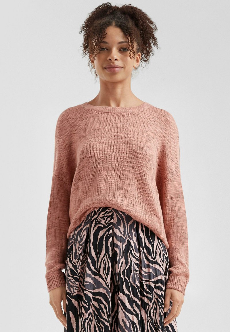 Maglione rosa lavorato a maglia con vestibilità morbida, tessuto strutturato e polsini a coste, abbinato a una gonna plissettata con motivo zebra nero e rosa.