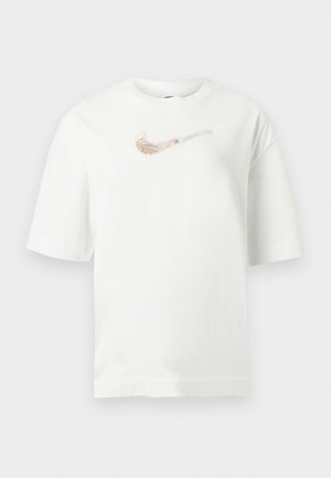Tricou alb cu mâneci scurte, cu logo-ul Nike swoosh auriu roz metalic centrat pe piept pe un fundal gri deschis.