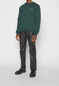 Ciemnozielona bluza z okrągłym dekoltem, ściągaczami na rękawach i dole. W zestawie z czarnymi skórzanymi spodniami i masywnymi czarnymi butami. Prosty design.