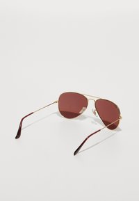 Aviatorsolbriller med guldmetalramme, brune tonede linser og maroon-accentuerede tempeltips. Letvægts og slankt design.