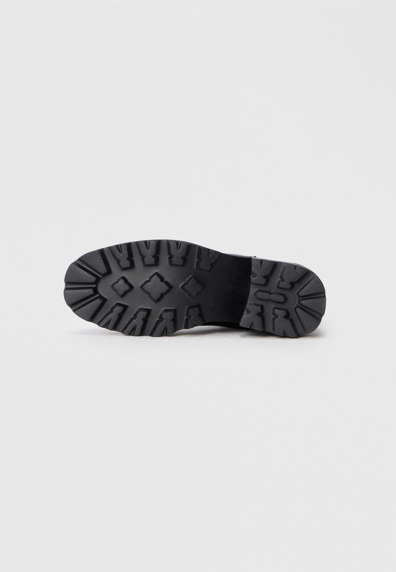 Suela de goma negra de una bota con patrones de relieve profundos diseñados para ofrecer tracción, mostrada de forma plana sobre un fondo blanco liso.