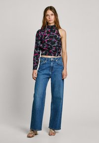 Top corto a fiori nero e rosa con manica lunga asimmetrica, abbinato a jeans larghi blu e sandali metallici con strappi.