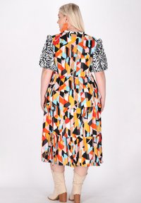 Ruha színes geometriai mintával, rétegekkel, rövid puffos ujjakkal, fekete-fehér mintázattal, valamint bézs magassarkú csizmával.