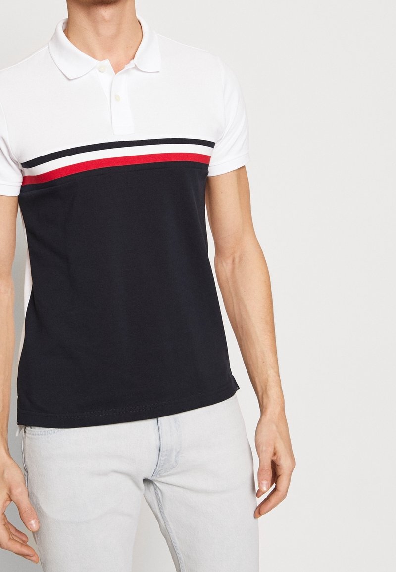 Polo à manches courtes avec un col blanc, corps navy et rayures horizontales rouges et blanches sur la poitrine. Matière en coton, coupe décontractée.