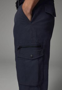 Marinefarbene Cargo-Shorts mit Seitentasche, Reißverschluss und gestickten Akzenten. Hergestellt aus leichtem Stoff mit glatter Textur.